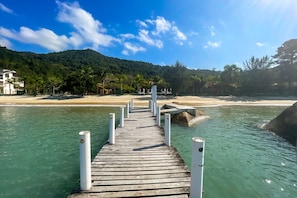 A wooden pier leading to a beach with clear water and a mountain in the background. - Pousada Recanto das Flores (Governador Celso Ramos)