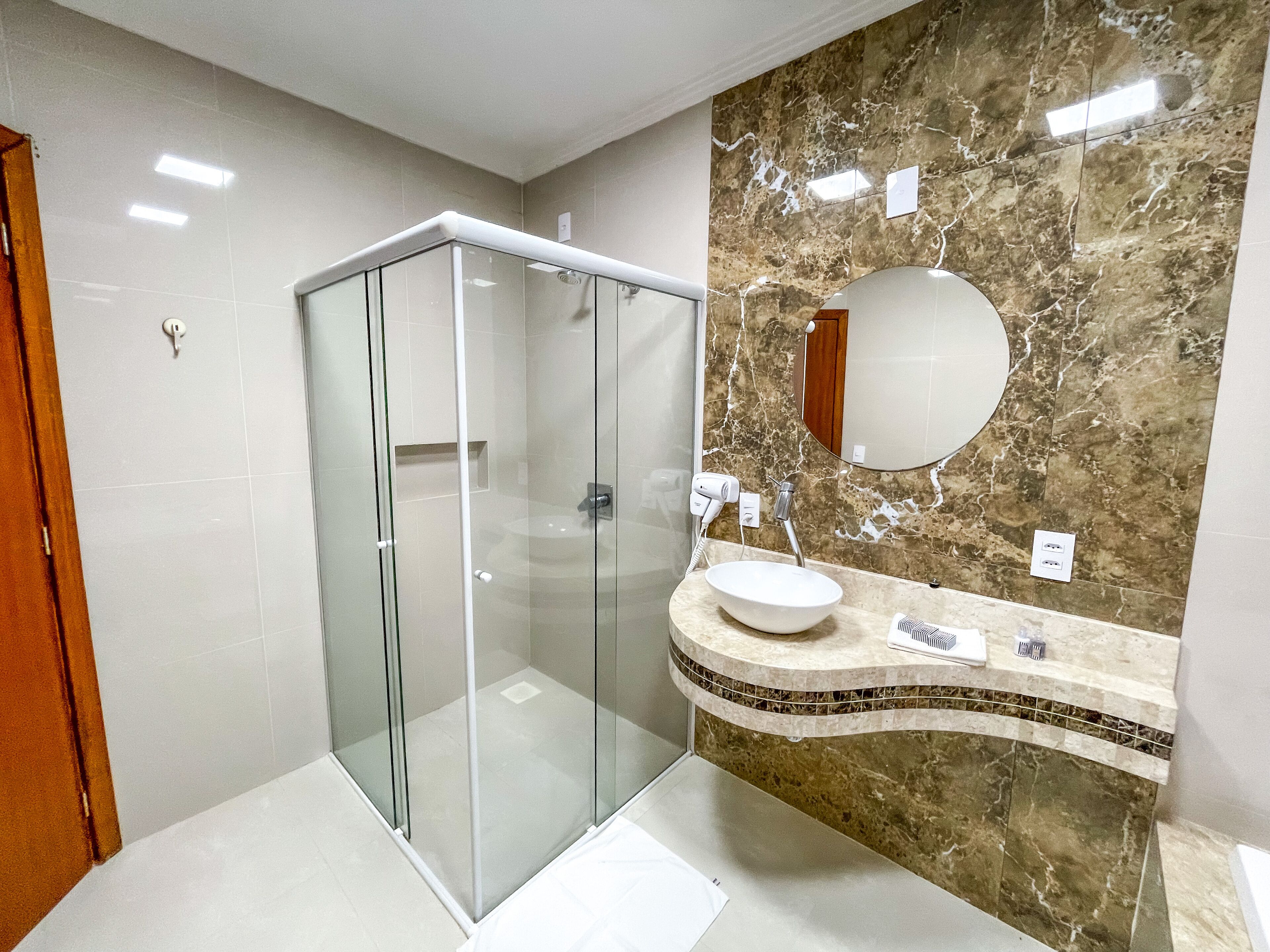 A modern bathroom with a glass-enclosed shower, a marble vanity, and a large mirror.