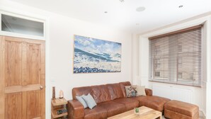 A living room with a brown leather sofa, a wooden coffee table, and a painting of a snowy landscape on the wall. - St Stephen Street Apartment (Edinburgh)