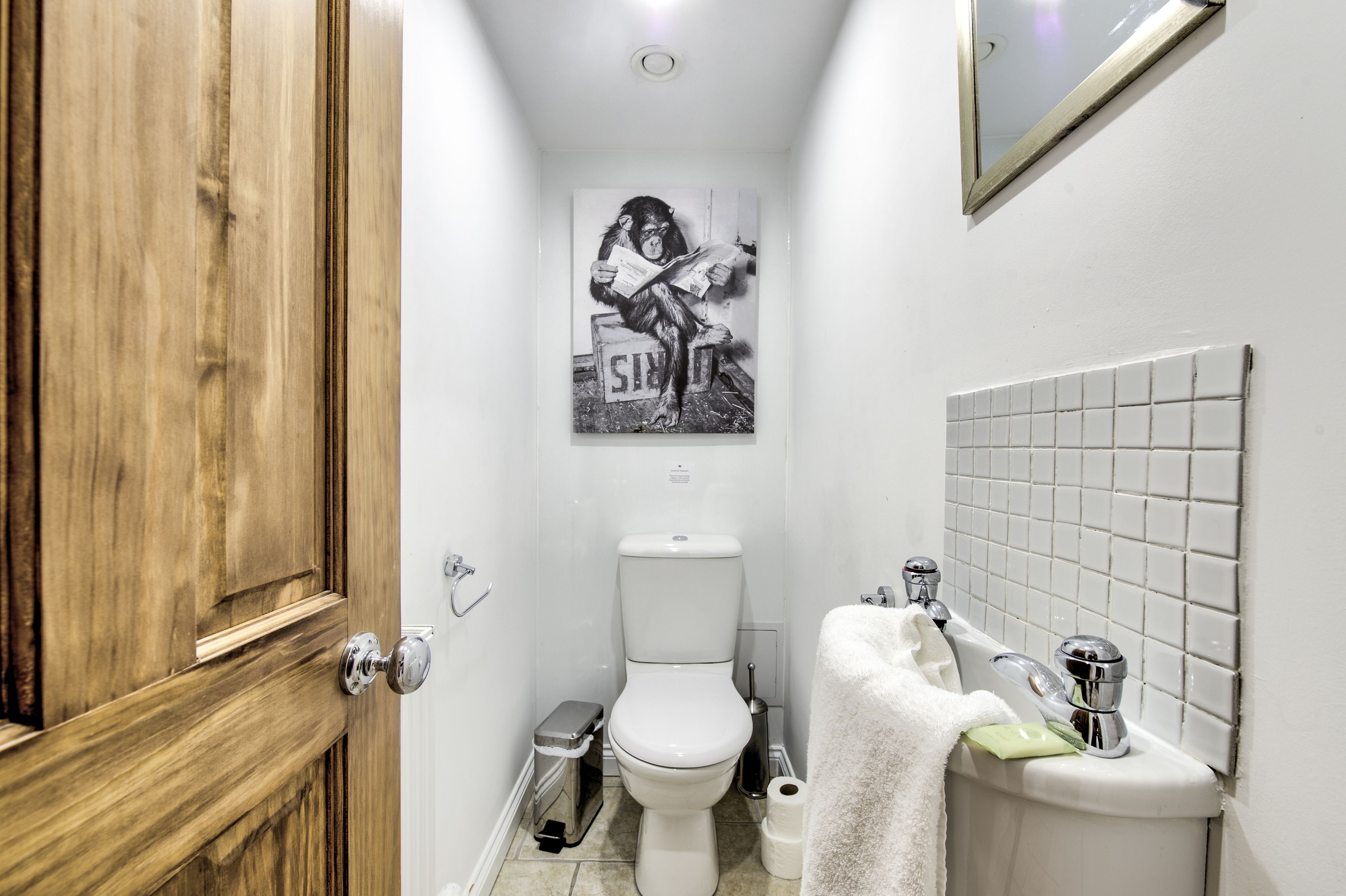 A narrow bathroom with a wooden door, a toilet, a sink with a towel, and a mirror on the wall.