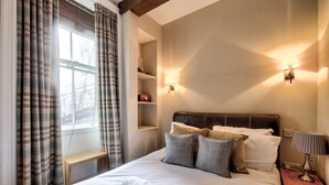 A neatly made bed with pillows, a bedside table, a lamp, and a shelf with items. - St Stephen Street Apartment (Edinburgh)