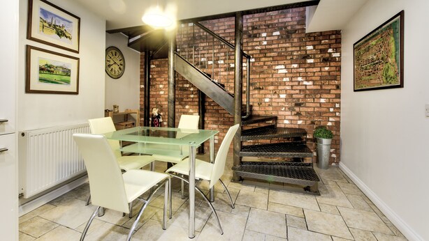 A dining area with a glass table and chairs, a brick wall, and a staircase. - St Stephen Street Apartment (Edinburgh)