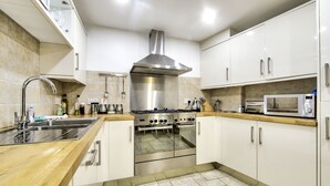 A modern kitchen with white cabinets, a stainless steel range hood, a built-in oven, a microwave, and a wooden countertop. - St Stephen Street Apartment (Edinburgh)