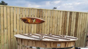 A wooden hot tub with a wooden deck and a wooden fence in the background. - Melorne Farm (Camelford)