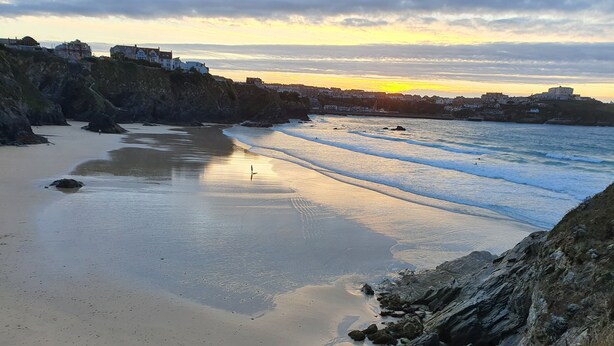 A coastal landscape with a beach, rocky cliffs, and buildings in the background. - Melorne Farm (Camelford)