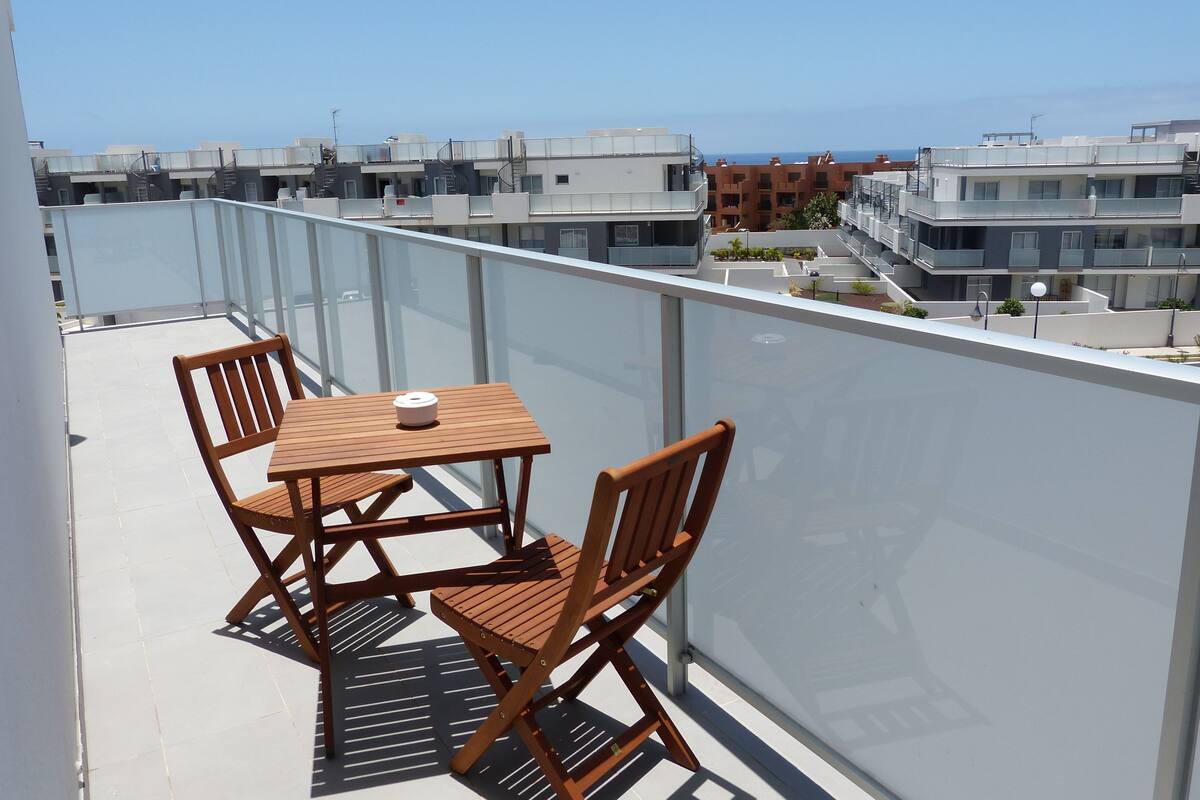 Ein Balkon mit Holztisch und -stühlen mit Blick auf ein Wohngebiet mit modernen Gebäuden.