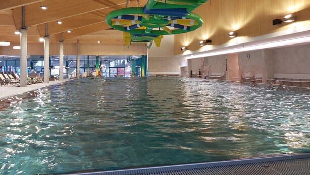 Piscina interior con agua cristalina, vigas de techo de madera y vistas al exterior a través de amplios ventanales.