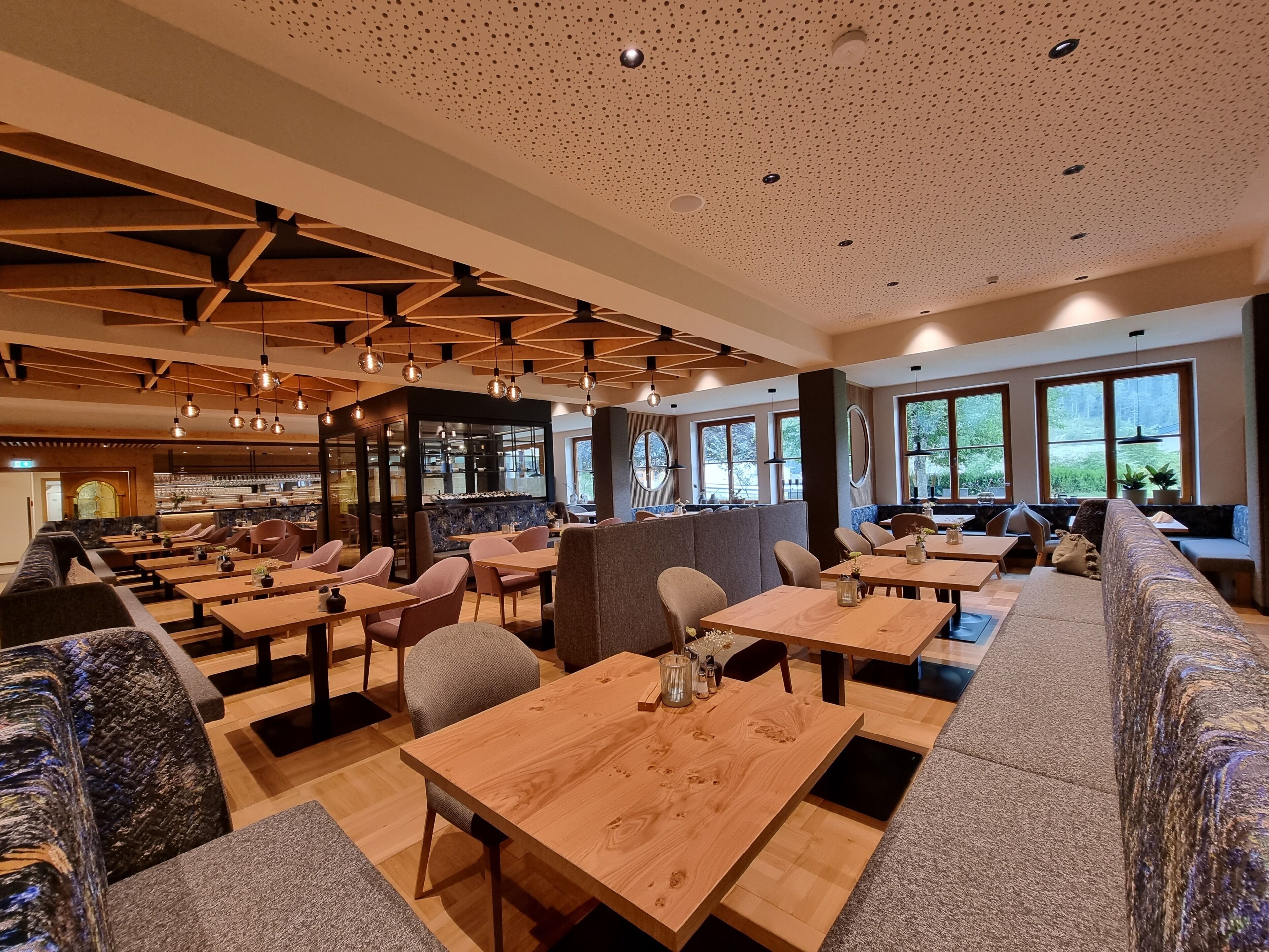 Un interior de restaurante moderno con mesas y sillas de madera, una zona de bar y ventanas amplias.