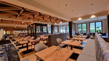 Un interior de restaurante moderno con mesas y sillas de madera, una zona de bar y ventanas amplias.