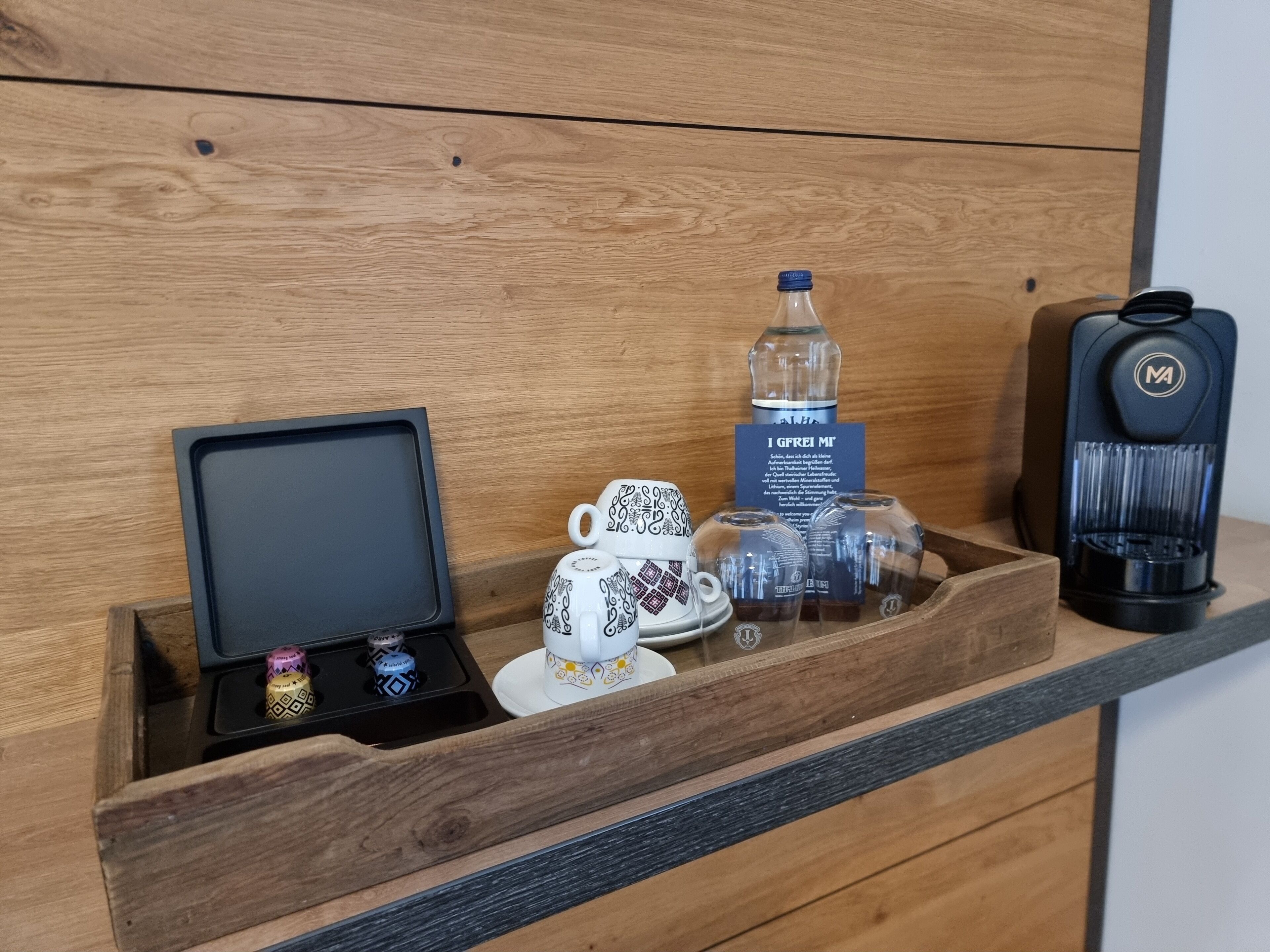 Un plateau en bois sur lequel sont posés une machine à café, une bouteille d’eau et une tasse, le tout sur une surface en bois.