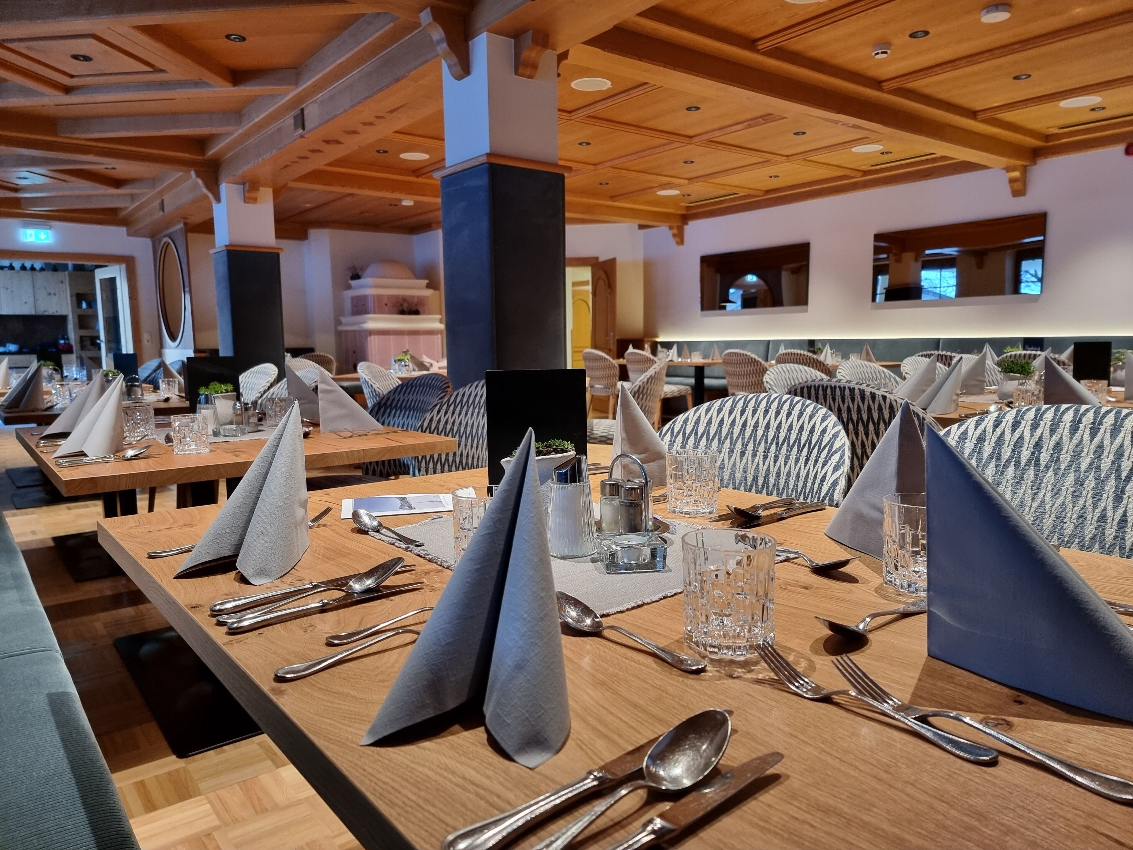 Un restaurante con mesas de madera dispuestas para comer, con servilletas, cubiertos y vasos.