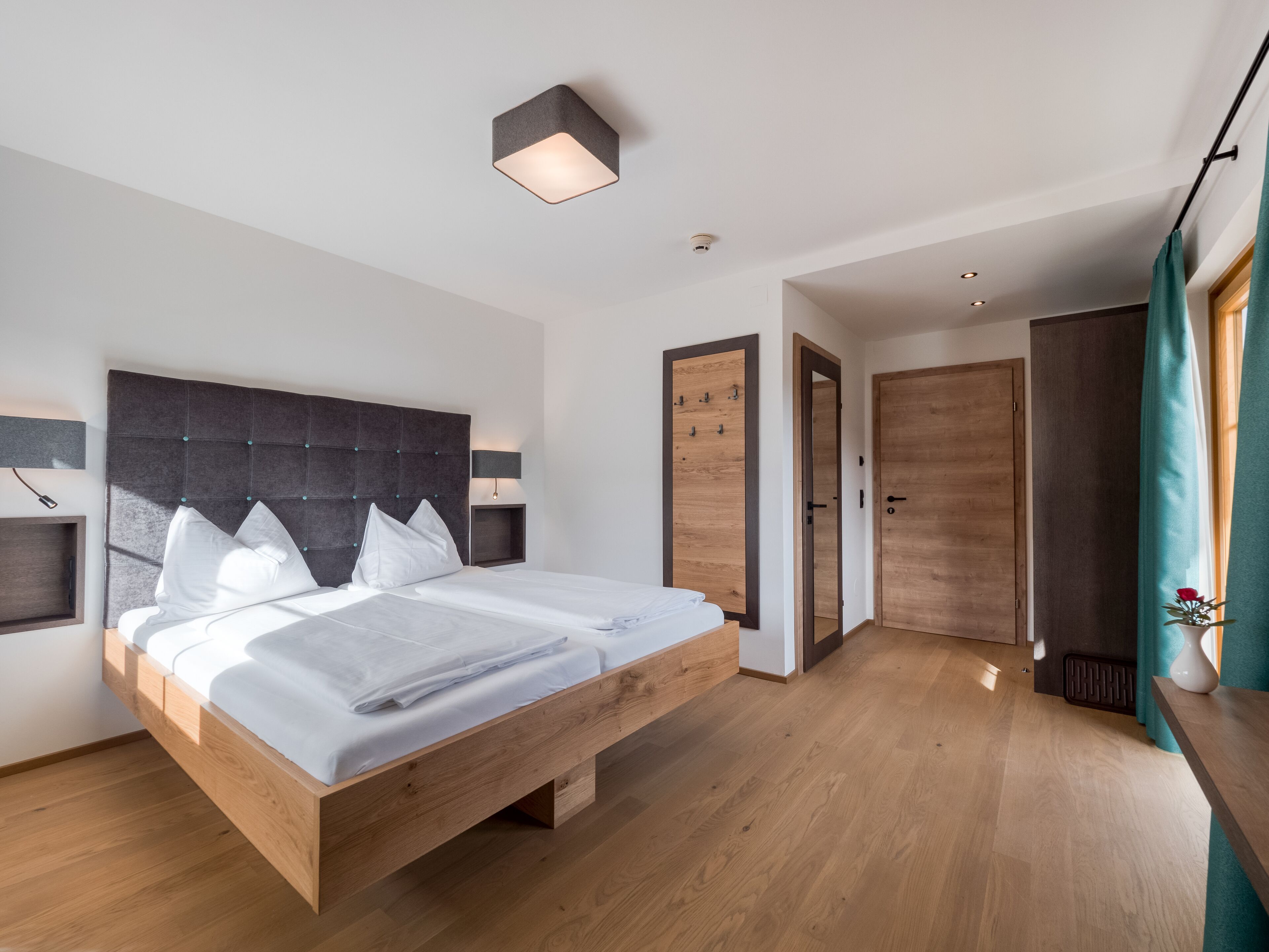 Un dormitorio moderno con una cama de madera, cabecera con lámpara y mesita de noche, además de un armario.
