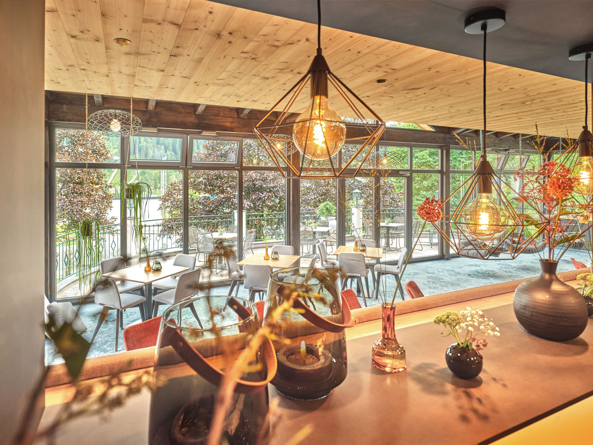Un comedor moderno con techo de madera, ventanas amplias y lámparas colgantes.