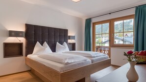 Habitación de hotel moderna con una cama grande, cabecera de madera y vistas a un paisaje montañoso a través del ventanal.