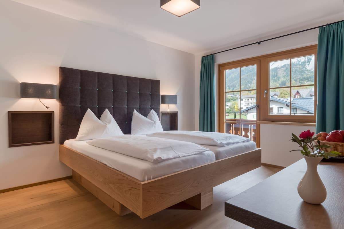 Habitación de hotel moderna con una cama grande, cabecera de madera y vistas a un paisaje montañoso a través del ventanal.