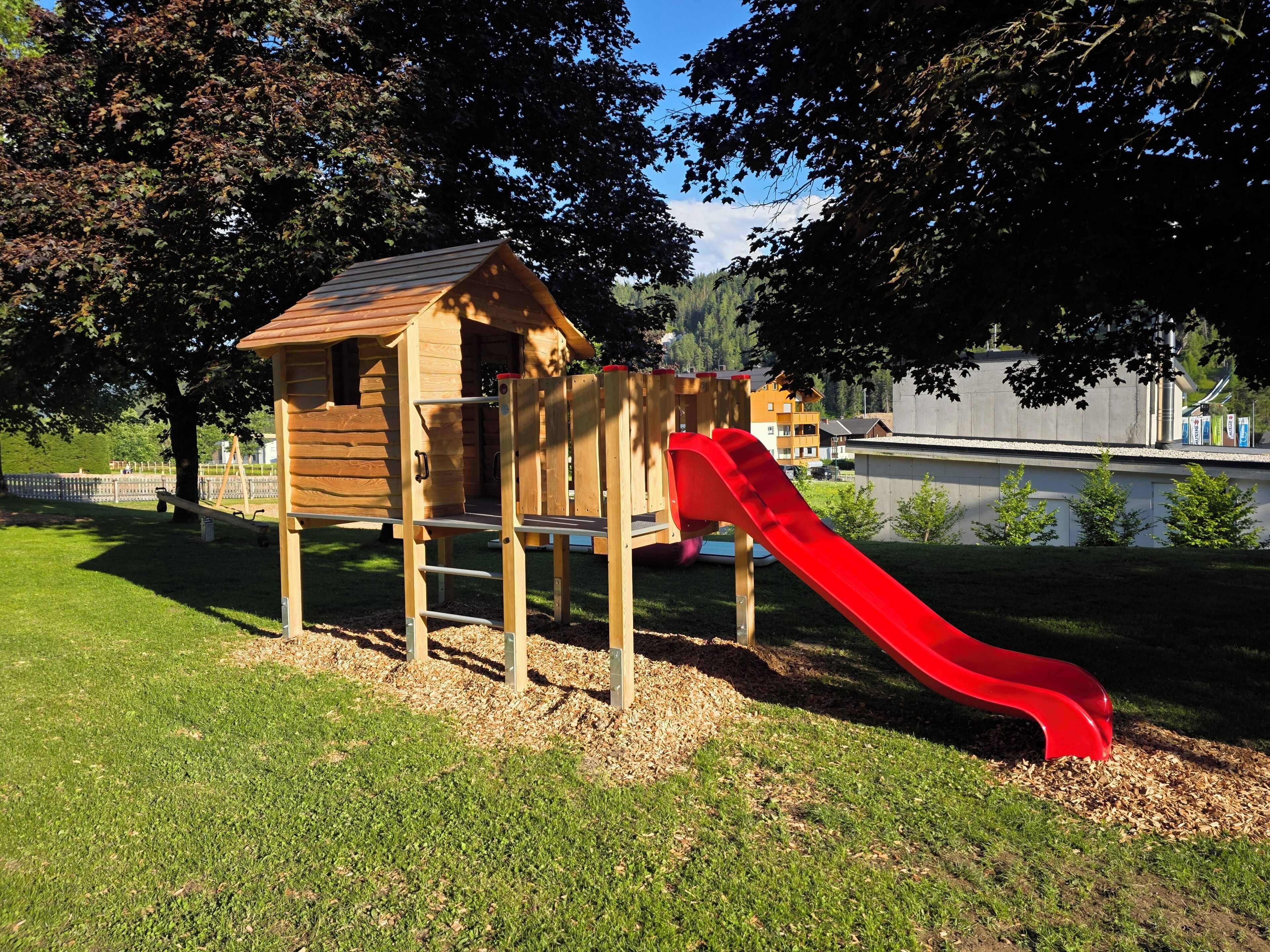 A wooden play structure with a red slide in a park.