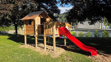 A wooden play structure with a red slide in a park.