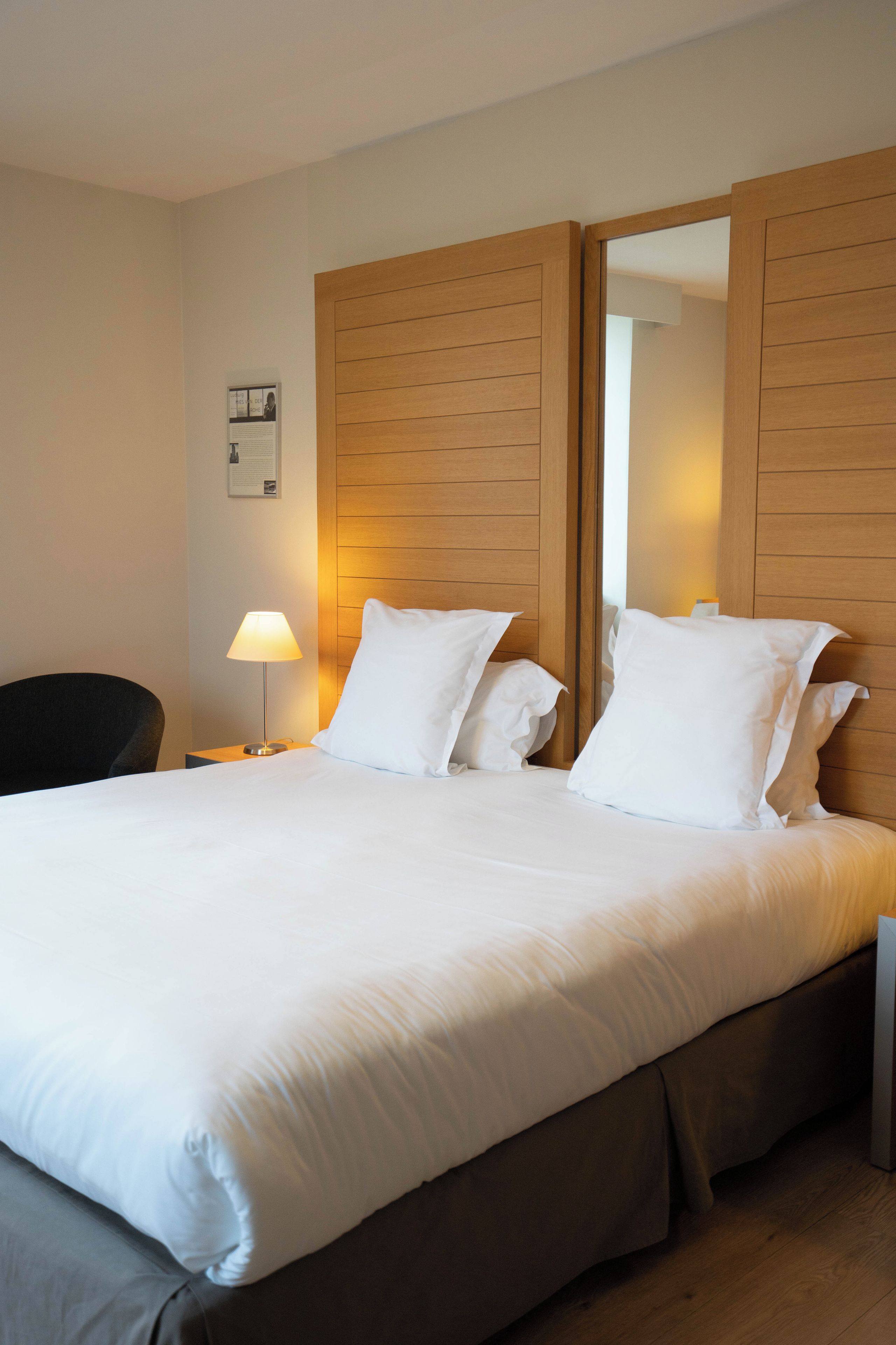 Habitación de hotel con una cama grande, una mesita de noche con lámpara y un espejo en la pared.