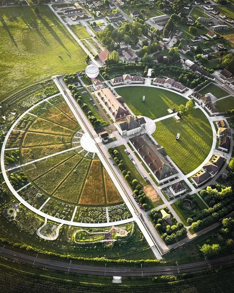 Vista aérea de un parque circular con una fuente central, rodeado de edificios residenciales y una carretera.