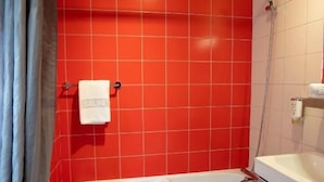 Un baño con azulejos rojos, una bañera blanca, una ducha y un taburete de madera.