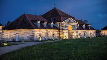 A historic stone building with multiple gabled roofs, a central entrance, and a well-maintained lawn.