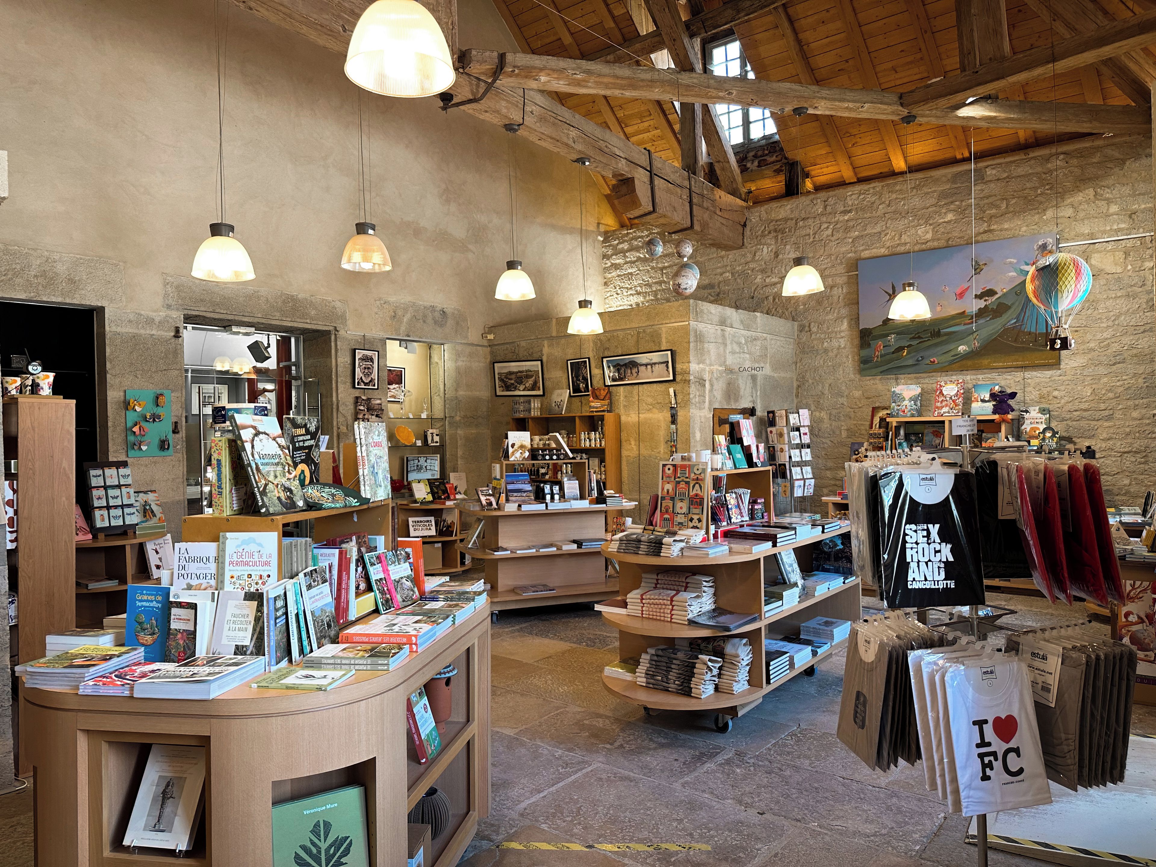 Une librairie avec des étagères en bois, des lampes suspendues et un mur en pierre rustique.