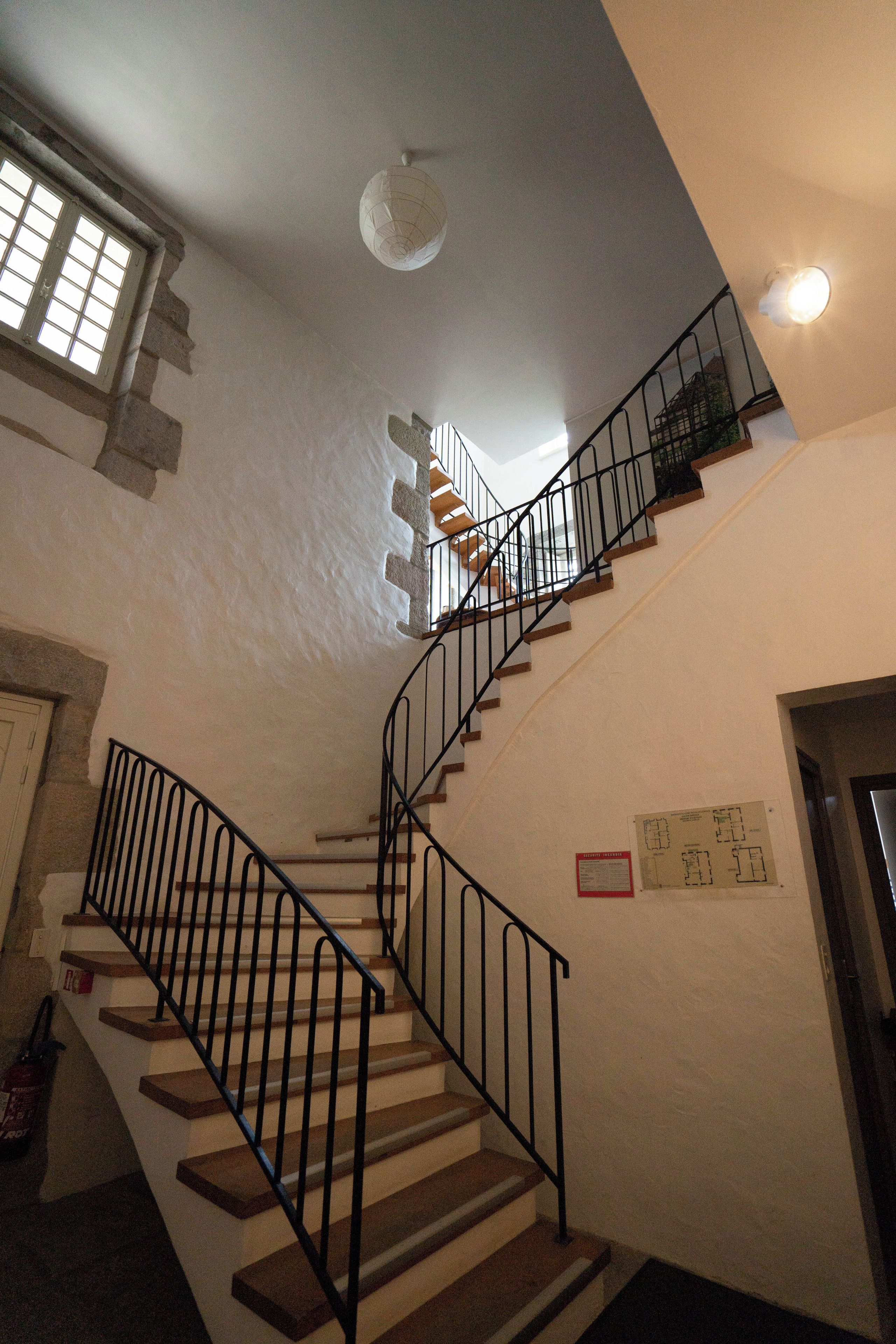 Un escalier avec une rampe en métal, un luminaire au plafond et une fenêtre à carreaux.
