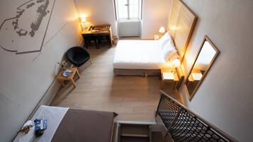 A hotel room with a bed, a desk, a chair, a small table, a window, and a wall with a map.