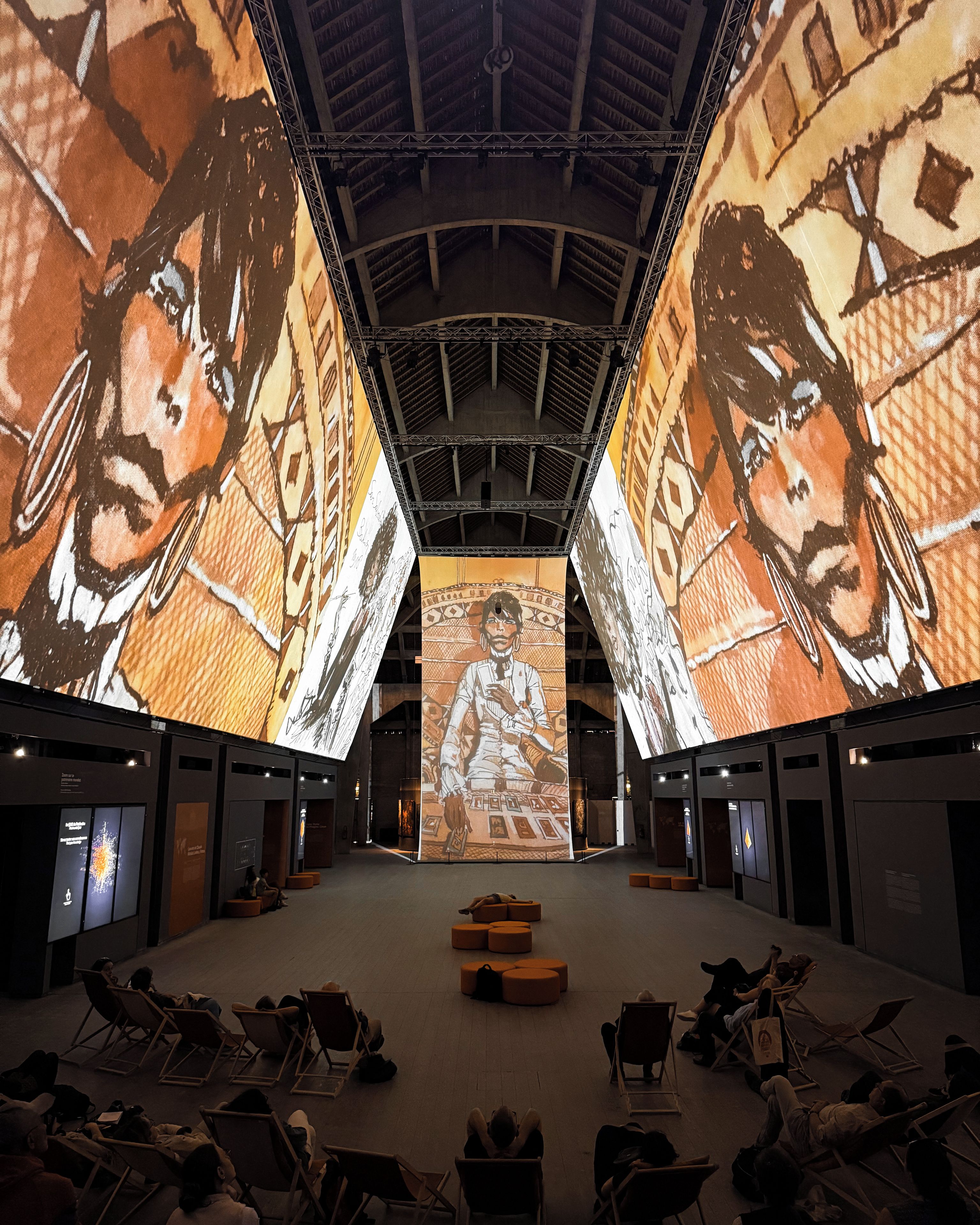 Un amplio salón con techo alto y pantallas digitales de gran tamaño que muestran obras de arte.