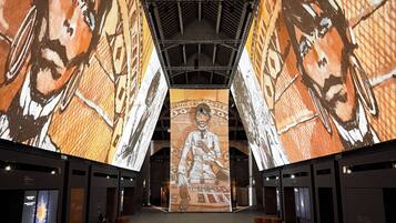 Un amplio salón con techo alto y pantallas digitales de gran tamaño que muestran obras de arte.