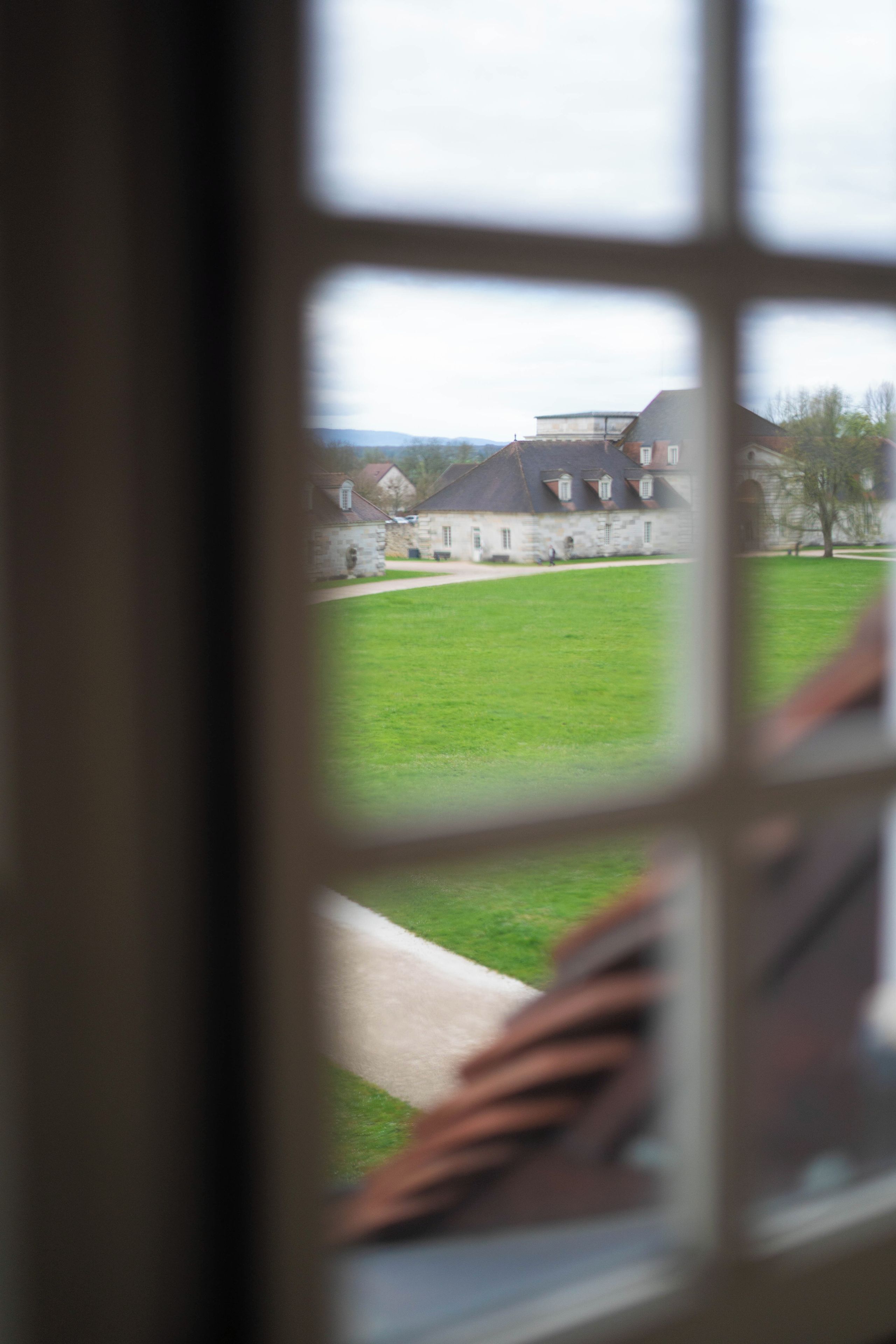 A view through a window of a building with a green lawn and a stone facade.