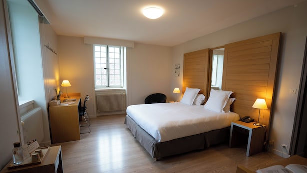 Una habitación de hotel con una cama, mesitas de noche, un escritorio, una silla, un radiador, una ventana y una puerta.