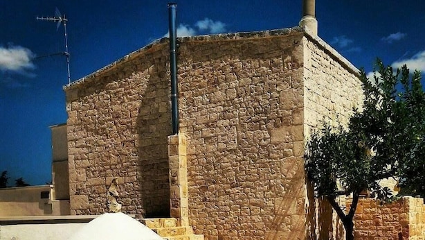 A stone building with a chimney, a staircase leading to a door, and a tree nearby. - Agriturismo Monte Adamo (Conversano)