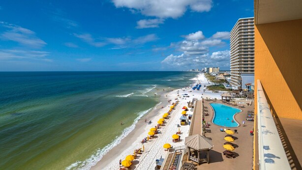 A beach view with a swimming pool, beach umbrellas, and a hotel building.