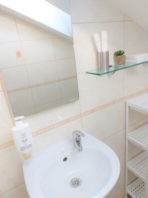 A bathroom with a white sink, a mirror, a glass shelf with toiletries, and a potted plant. - Apartment Tina (Dubrovnik)