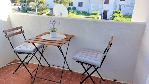 A small balcony with two wooden chairs, a table, and a potted plant.