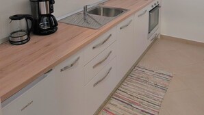 A compact kitchen with white cabinets, a microwave, a coffee maker, a sink, and an oven.