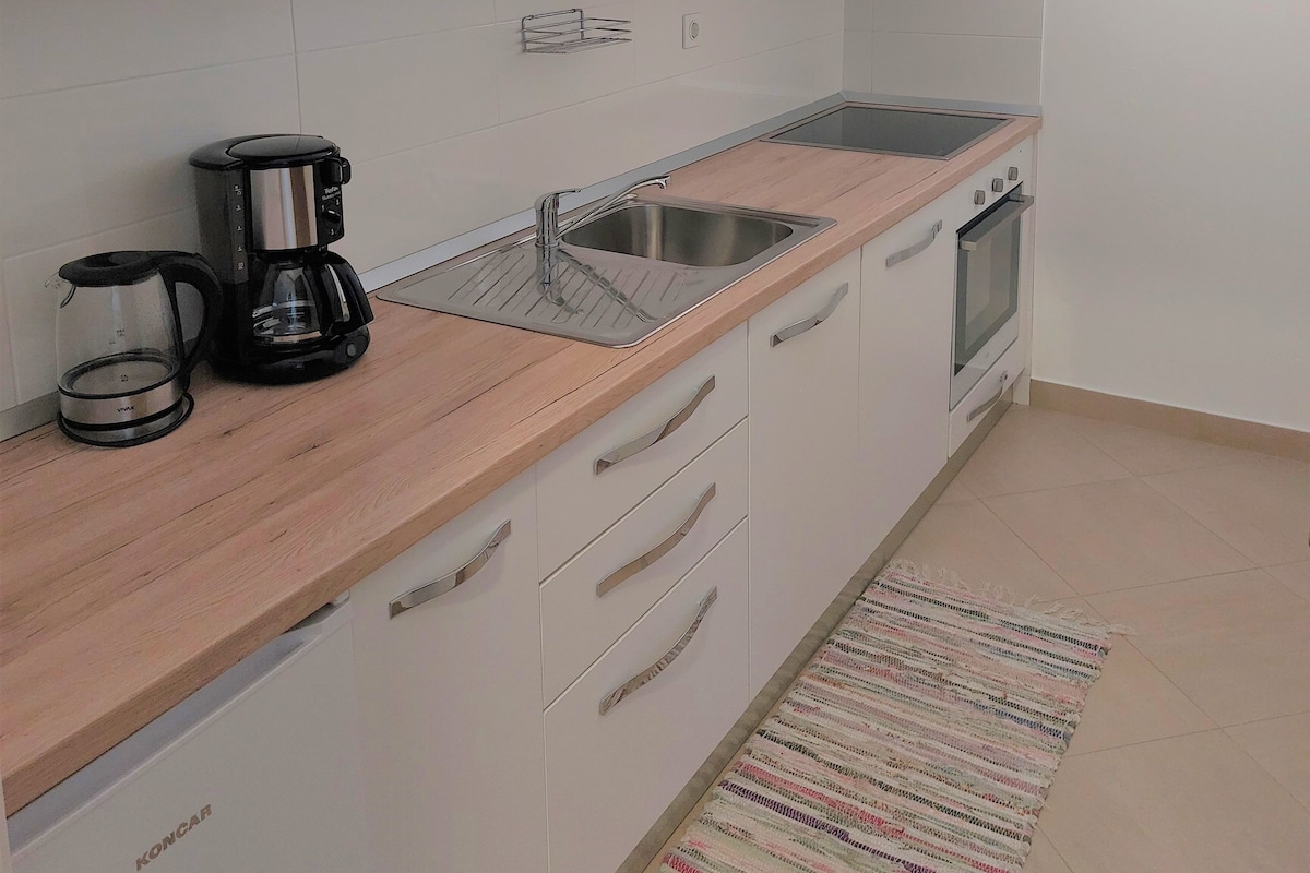 A compact kitchen with white cabinets, a microwave, a coffee maker, a sink, and an oven.