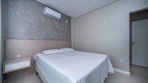 Een slaapkamer met een bed, nachtkastje, airconditioning en een deur.