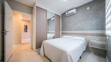 Quarto de hotel com cama, mesas de cabeceira, aparelho de ar condicionado e uma porta que dá para outro quarto.