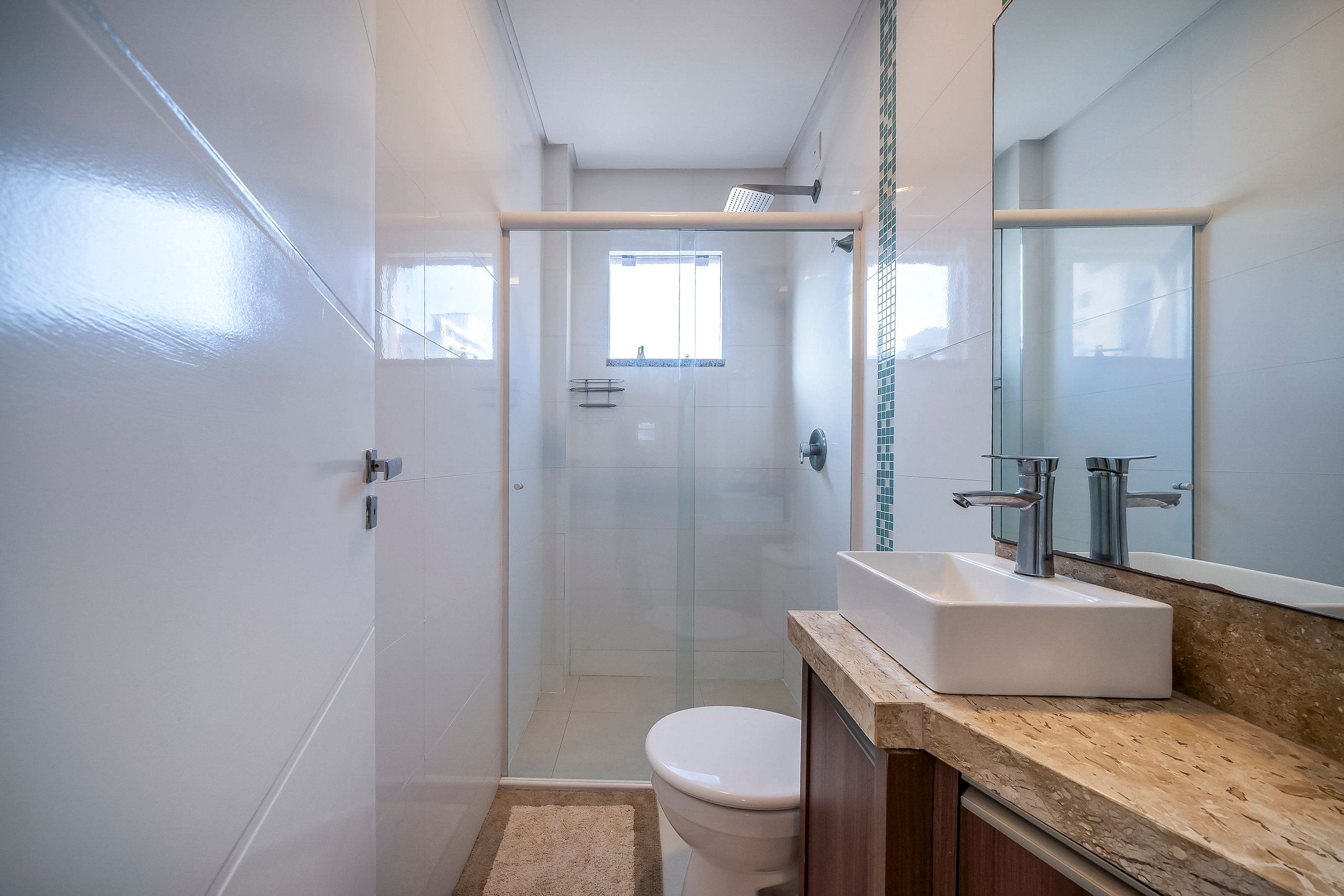 A bathroom with a glass shower enclosure, a toilet, and a sink with a mirror above it.