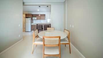 Uma área de refeições com uma mesa redonda e quatro cadeiras, uma cozinha ao fundo, e uma paleta de cores neutras.