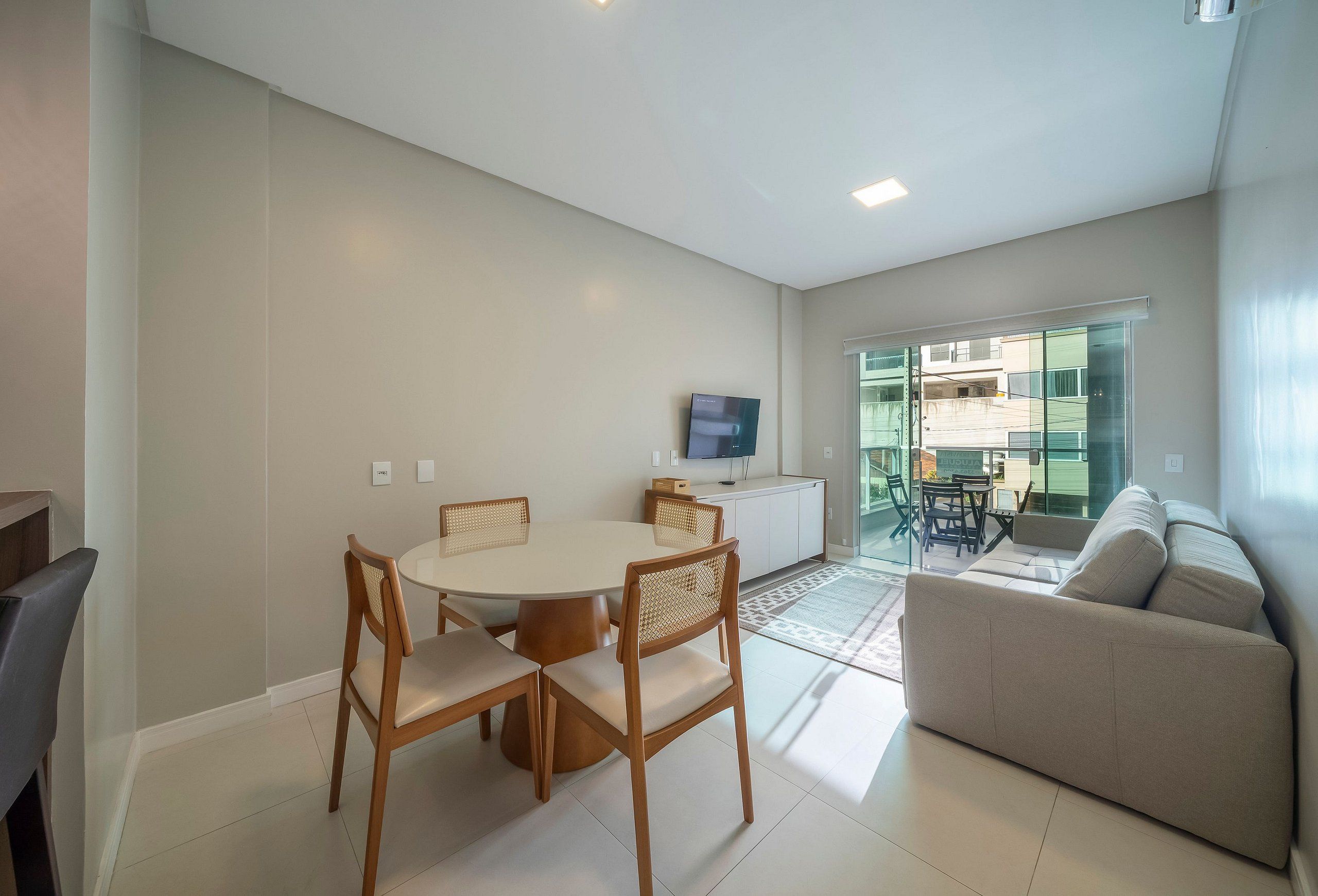 Un salon moderne comprenant un canapé, une table à manger avec des chaises, un téléviseur à écran plat fixé au mur et une porte vitrée donnant sur un espace extérieur.