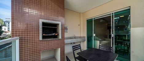 An outdoor patio with a barbecue grill, a table with chairs, and a sliding glass door leading to a balcony.