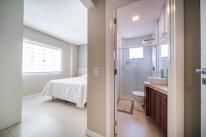 Um quarto com cama e banheiro com chuveiro e pia.