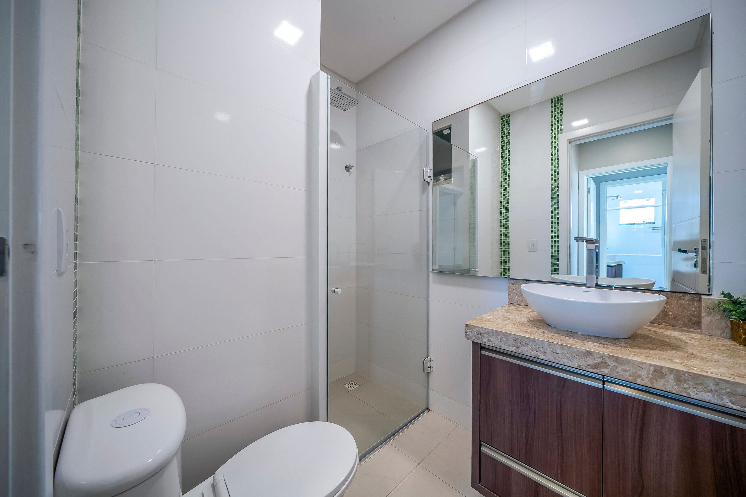 A modern bathroom with a glass shower enclosure, a white toilet, and a vanity with a large mirror and a vessel sink.