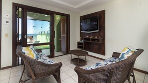 A living room with wicker furniture, a television mounted on the wall, and a glass door leading to an outdoor area.