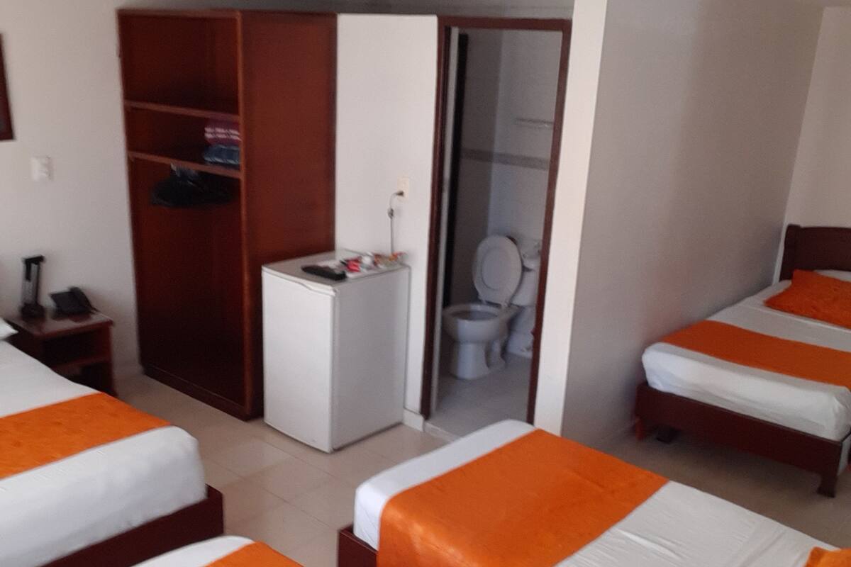 Une chambre d’hôtel avec trois lits, une armoire, un petit bureau et des toilettes.