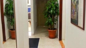 Un pasillo con suelo de baldosas, plantas en macetas, una puerta al final y un cuadro en la pared.