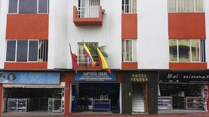 Un edificio con una entrada central, un balcón pequeño y tres escaparates visibles: una peluquería, un centro óptico y un centro hotelero.